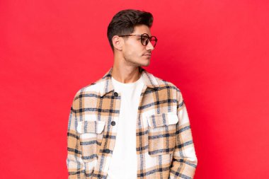 Genç, beyaz, yakışıklı bir adam, kırmızı arka planda izole edilmiş, yana bakıyor.