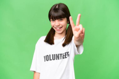 Küçük gönüllü kız izole edilmiş arka planda gülümsüyor ve zafer işareti gösteriyor.