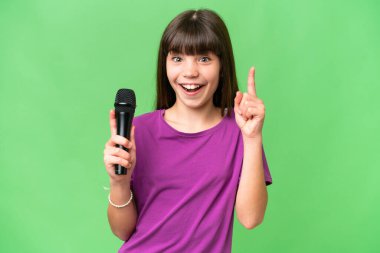 Küçük şarkıcı kız izole edilmiş bir arka planda mikrofonu eline alıp harika bir fikri işaret ediyor.