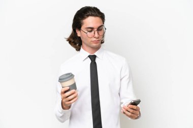 Beyaz arka planda izole edilmiş yakışıklı bir iş adamı elinde kahve ve bir cep telefonu tutuyor.