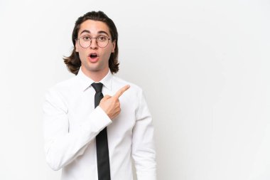 Beyaz arka planda izole edilmiş yakışıklı iş adamı şaşırmış ve işaret ediyor.