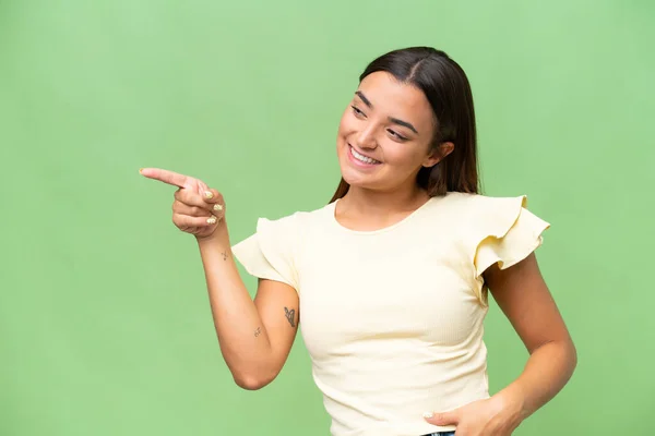 緑のクロマを背景に指を横に向けて製品を提示する若い白人女性 — ストック写真