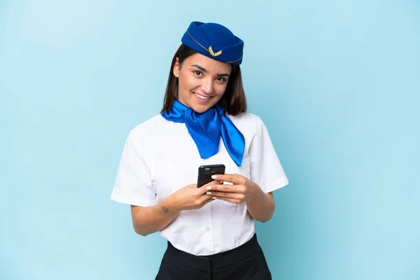 青い背景に隔離された飛行機スチュワーデス原因アジアの女性は 携帯電話でメッセージを送信します — ストック写真
