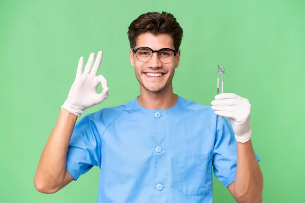 Jovem Dentista Homem Segurando Ferramentas Sobre Fundo Isolado Mostrando Sinal — Fotografia de Stock