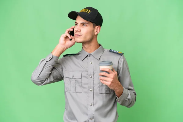 Giovane Uomo Sicurezza Sfondo Isolato Tenendo Caffè Portare Cellulare — Foto Stock