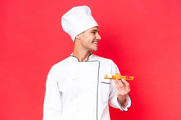 赤い背景に孤立した刺身を持つ若い白人料理人 — ストック写真