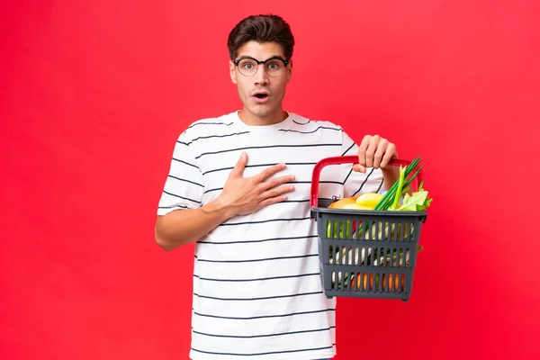 Mladý Běloch Muž Drží Nákupní Košík Plný Potravin Izolovaných Červeném — Stock fotografie