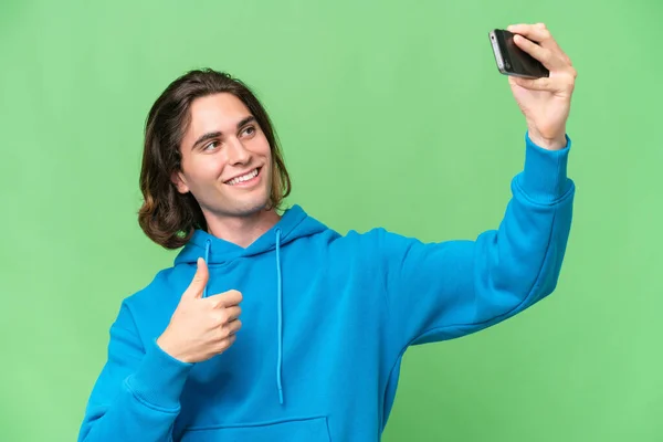 年轻英俊的男人被绿色的背景隔离 用手机制造了一个自拍 — 图库照片