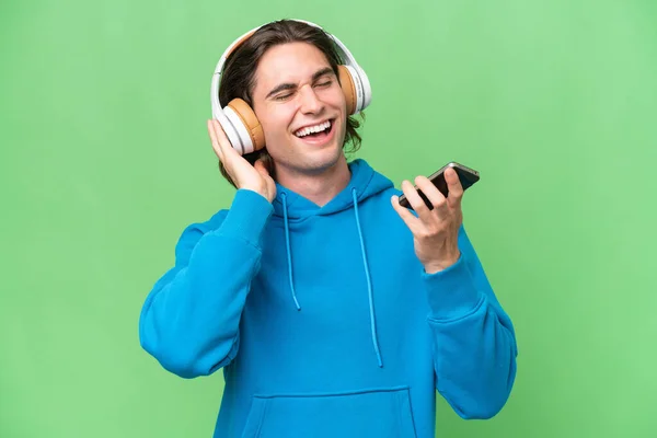 Молодий Красивий Чоловік Ізольований Зеленому Хромовому Фоні Слухаючи Музику Мобільним — стокове фото
