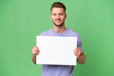 Sarışın, beyaz bir adam izole edilmiş bir arka planda elinde mutlu bir ifadeyle boş bir levha tutuyor.