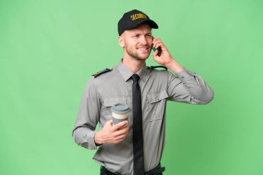 İzole edilmiş arka planda genç bir beyaz adam kahve ve cep telefonu tutuyor.