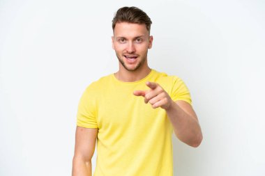 Beyaz arka planda izole edilmiş genç sarışın beyaz adam şaşırmış ve ön tarafı işaret ediyor.