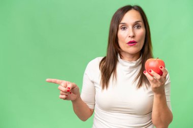 Orta yaşlı beyaz kadın, yeşil arka planda elma tutarken izole edilmiş.