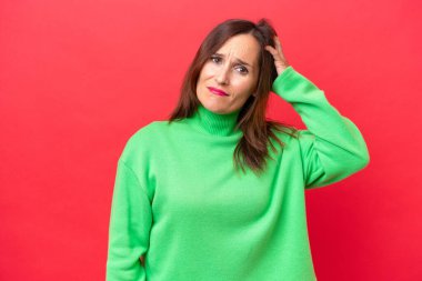 Orta yaşlı, beyaz bir kadın. Kırmızı arka planda izole edilmiş. Hüsrana uğramış ve anlamamış.