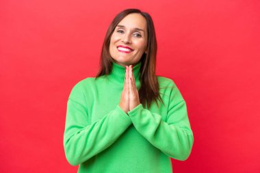 Kırmızı arka planda izole edilmiş orta yaşlı beyaz kadın avuç içlerini bir arada tutuyor. İnsan bir şey ister.