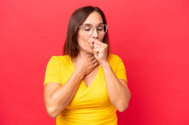 Orta yaşlı beyaz kadın, kırmızı arka planda izole edilmiş, çok öksürüyor.