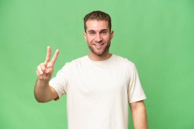 Yeşil krom arka planda izole edilmiş yakışıklı beyaz adam gülümsüyor ve zafer işareti gösteriyor.