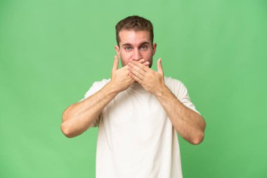 Yeşil krom arka planda izole edilmiş yakışıklı, beyaz bir adam elleriyle ağzını kapatıyor.