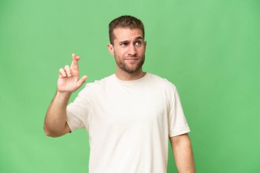 Yeşil krom arka planda izole edilmiş yakışıklı beyaz bir adam. Parmakları çapraz ve en iyisini diliyor.