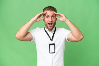 Kimlik kartı olan genç beyaz bir adam, yeşil renkli arka planda, sürpriz bir ifadeyle izole edilmiş.