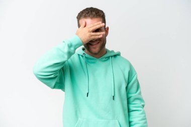 Beyaz arka planda soyutlanmış beyaz tenli yakışıklı bir adam. Gözleri elleriyle kaplıyor ve gülümsüyor.