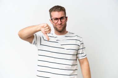 Beyaz arka planda izole edilmiş beyaz, yakışıklı beyaz bir adam, olumsuz bir ifadeyle baş parmağını aşağı gösteriyor.