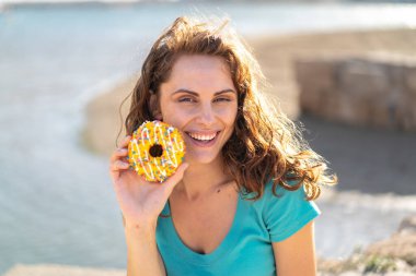 Genç sporcu kadın elinde donutla dışarıda gülümsüyor.