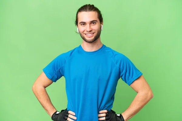 年轻英俊男子 背景为绿色 双手叉腰 面带微笑 — 图库照片