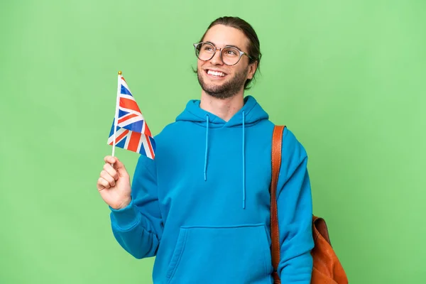 年轻英俊的男子举着英国国旗 身披孤立的背景 一边高瞻远瞩 一边思考问题 — 图库照片