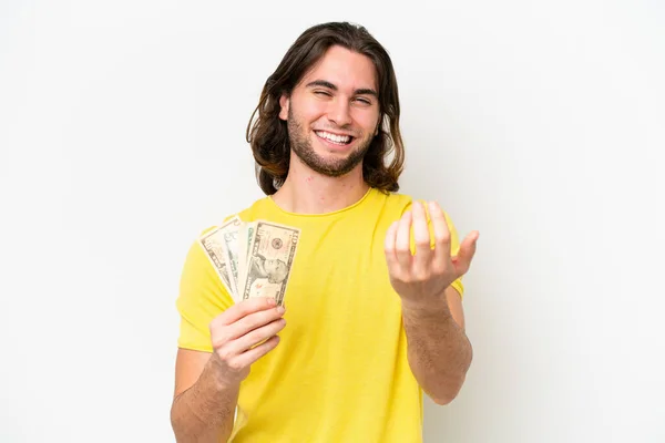 Young handsome man taking a lot of money isolated on white background inviting to come with hand. Happy that you came