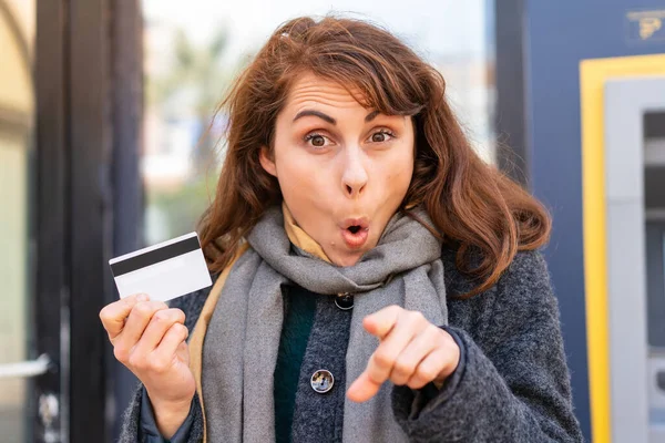 Mujer Morena Sosteniendo Una Tarjeta Crédito Aire Libre Sorprendida Apuntando —  Fotos de Stock