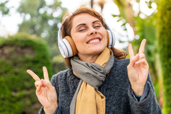 Μελαχρινή Γυναίκα Ακούγοντας Μουσική Ακουστικά Εξωτερικούς Χώρους Δείχνει Νίκη Υπογράψει — Φωτογραφία Αρχείου