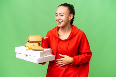 Genç bir Arap kadın arka planda fast food tutuyor ve gülümsüyor.