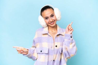 Mavi arka planda izole edilmiş kışlık kuklalar takan genç bir Arap kadını işaret ediyor ve mutlu.