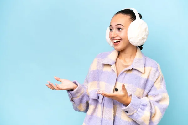 stock image Young Arab woman wearing winter muffs isolated on blue background with surprise facial expression