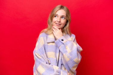 Young English woman isolated on red background looking up while smiling