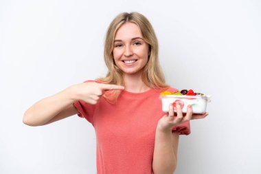 Genç İngiliz kadın izole edilmiş beyaz arka plan üzerinde bir kase meyve tutuyor ve onu işaret ediyor.