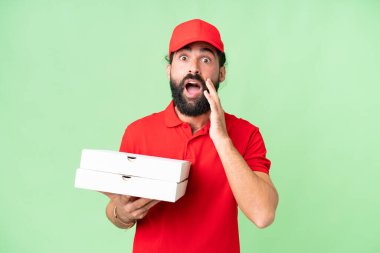 İş üniformalı bir pizzacı, izole edilmiş krom anahtar arka planda pizza kutuları alıyor. Şaşırmış ve şok olmuş yüz ifadesi var.