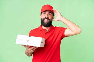 İş üniformalı bir pizzacı, izole edilmiş krom anahtar arkaplanından pizza kutuları alıyor. Sürpriz bir ifadeyle.