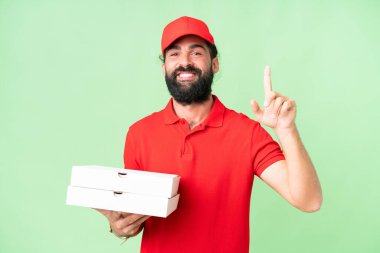 İş üniformalı bir pizzacı, izole edilmiş krom anahtar arkaplanından pizza kutularını alıyor ve en iyinin işareti olarak parmağını kaldırıyor.