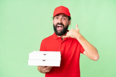 İş üniformalı bir pizzacı, izole edilmiş krom anahtar arkaplanda pizza kutularını topluyor ve telefon jesti yapıyor. Bana geri dönüş işareti ver.