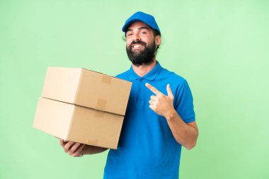 Delivery caucasian man over isolated chroma key background pointing to the side to present a product