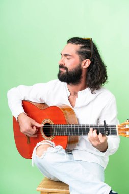 Young man with beard with guitar over isolated chroma key background