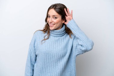 Beyaz arka planda izole edilmiş genç beyaz kadın elini kulağına koyarak bir şeyler dinliyor.