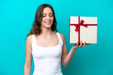 Elinde mavi arka planda mutlu bir ifadeyle izole edilmiş bir hediye tutan beyaz bir kadın.