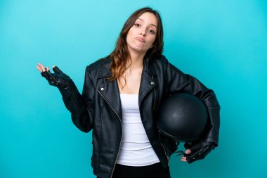 Young caucasian woman with a motorcycle helmet isolated on blue background having doubts while raising hands