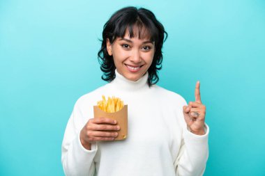 Arjantinli genç bir kadın elinde kızarmış cipslerle mavi arka planda harika bir fikre işaret ediyor.