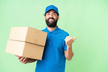 Delivery caucasian man over isolated chroma key background pointing to the side to present a product