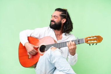 Young man with beard with guitar over isolated chroma key background