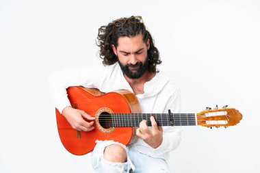 Beyaz arka planda gitar çalan sakallı genç bir adam.